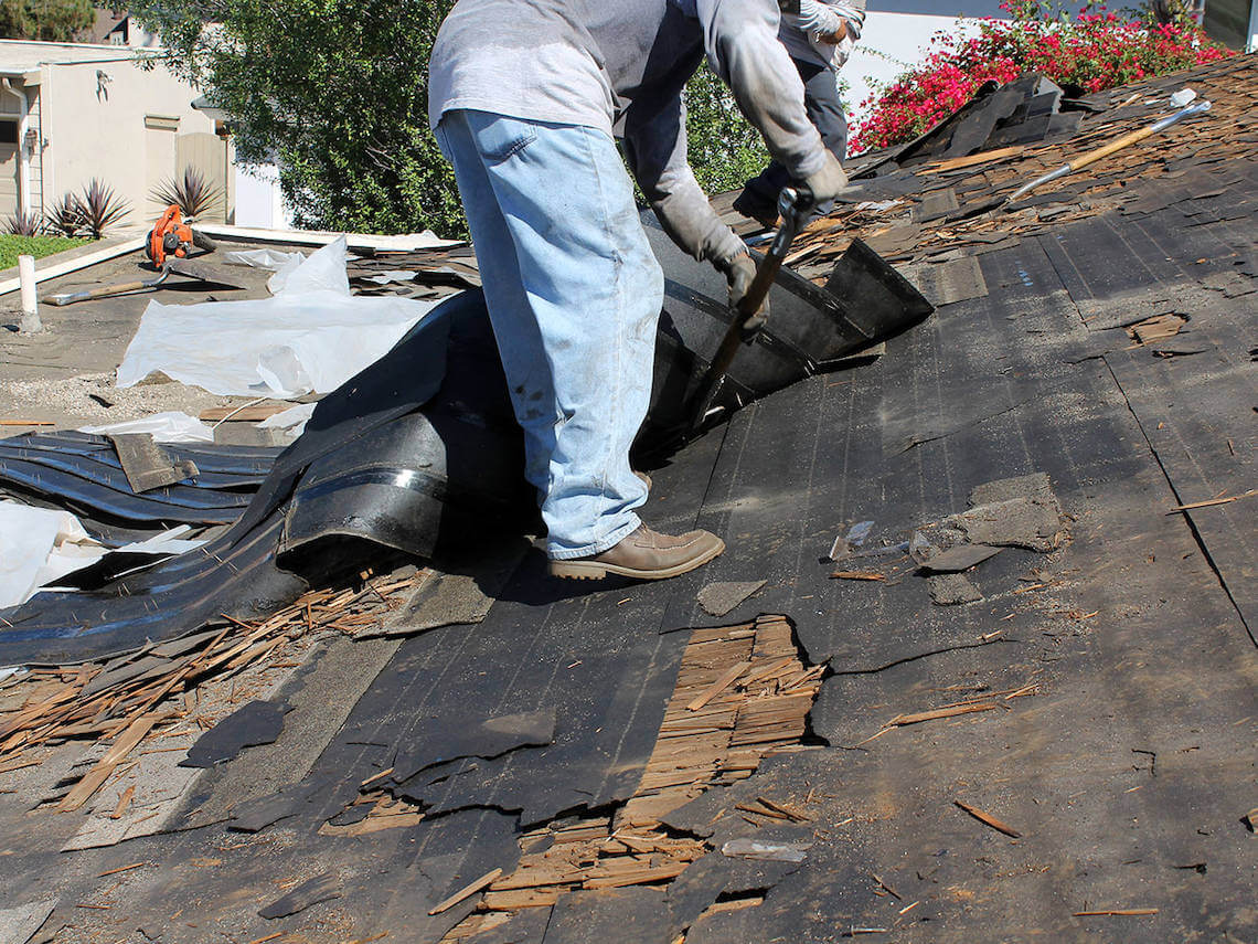 Roofer stripping old felt from a flat roof before recovering