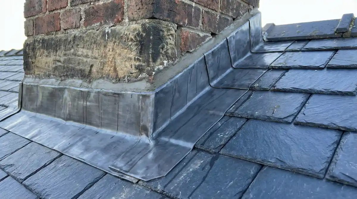 Lead flashing dressed around a brick chimney on a slate roof